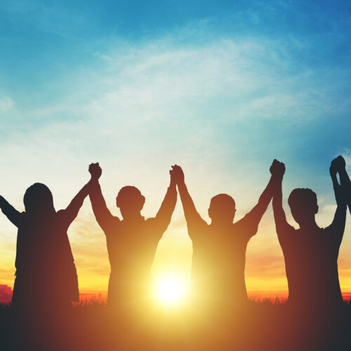 people holding hands and celebrating at sunset